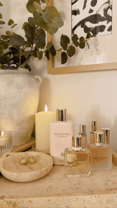 a candle lit display of Givenchy Irresistible perfume and makeup in a travertine tray on top of a dresser