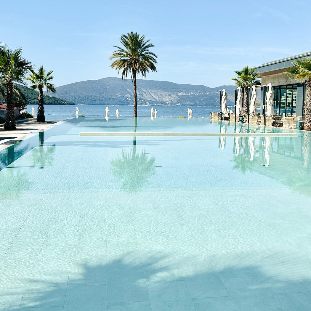 Scenic view overlooking luxury hotel pool with palm trees and hills in the background.